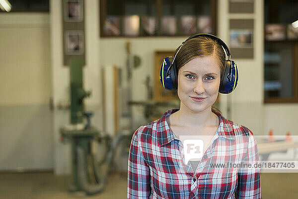 Smiling craftswoman wearing ear protectors in workshop