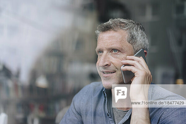 Lächelnder Mann  der durch ein Glasfenster auf einem Smartphone spricht