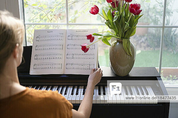 Woman with music sheets sitting in front of piano at home