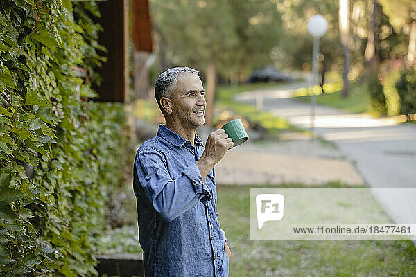 Mature man drinking coffee at overgrown facade