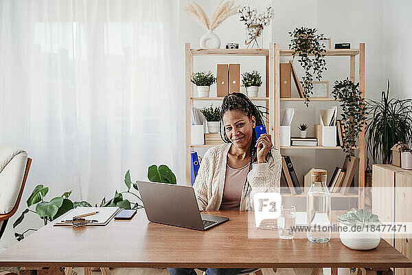 Lächelnder Freiberufler sitzt mit Kreditkarte und Laptop im Heimbüro