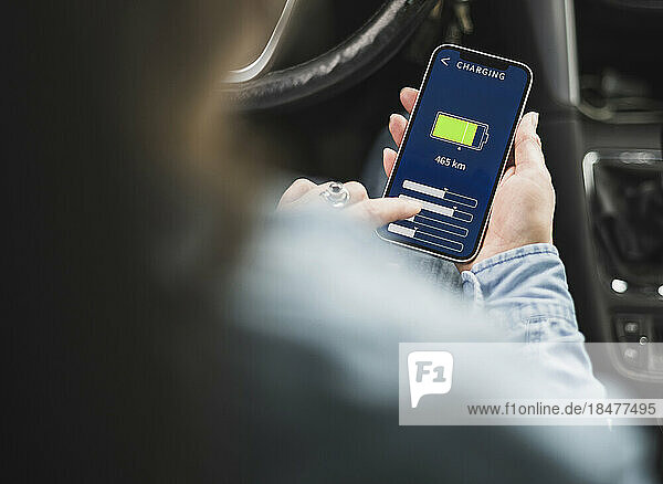 Hand of mature woman operating electric car through mobile app on smart phone