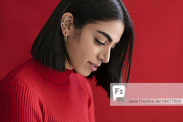 Shy young woman looking down against red background