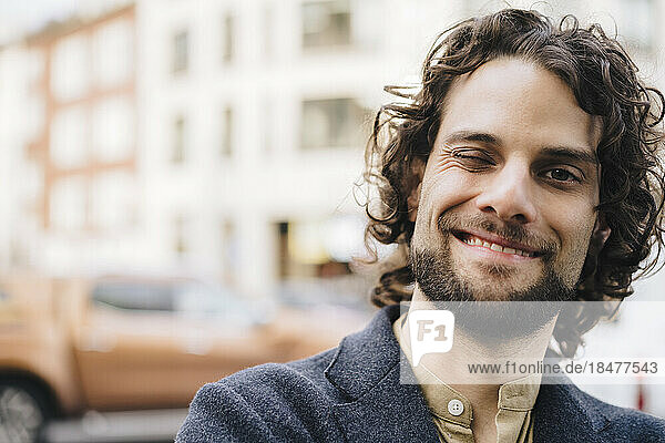 Happy young businessman with curly hair winking