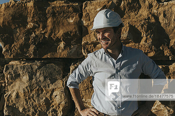 Happy architect with hands on hip standing in front of brick wall