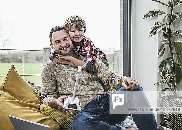 Smiling father and son with wind turbine model at home