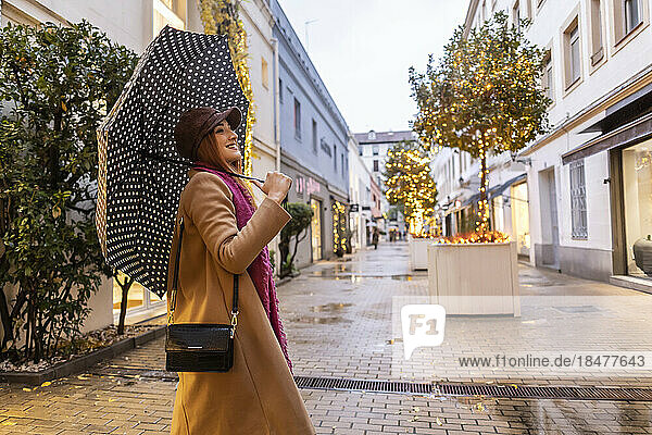 Smiling young woman with umbrella standing at footpath