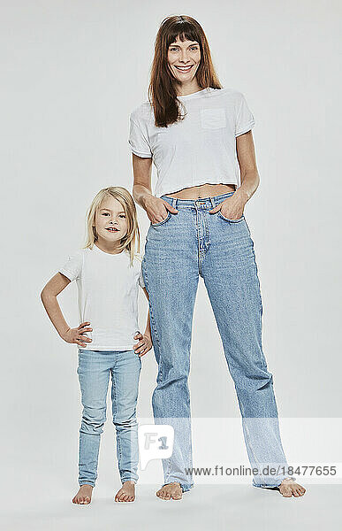 Lächelnde Mutter und Tochter mit der Hand auf der Hüfte vor weißem Hintergrund