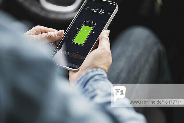 Hands of woman using mobile app to operate electric car