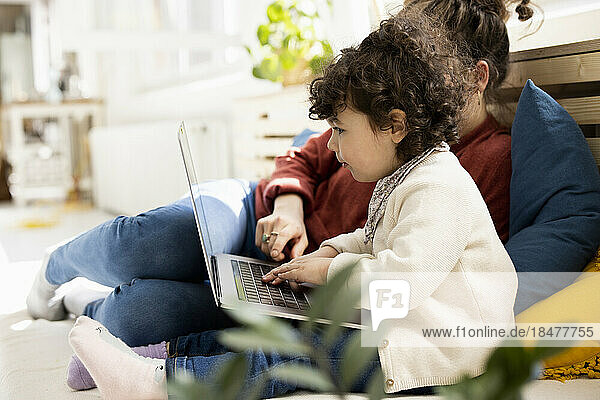Little girl using laptop sitting on lap of mother on couch at home