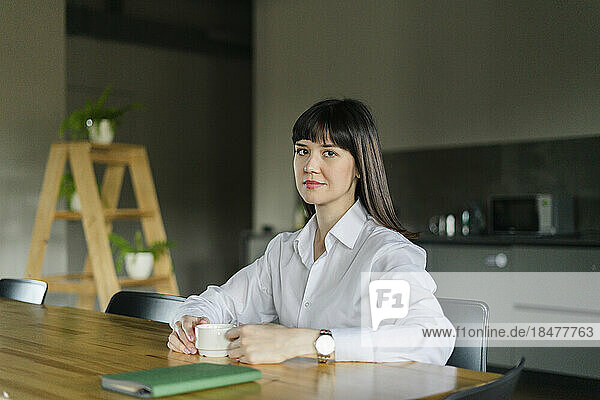 Portrait of brunette businesswoman sitting at table in office kitchen