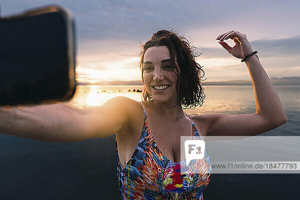 Happy woman taking selfie through smart phone at beach