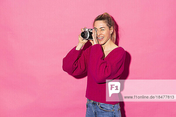 Happy woman taking photo with camera against pink background