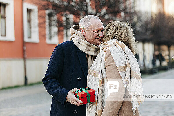 Senior man holding gift box standing with woman on street