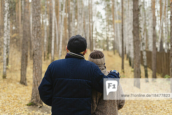Senior man with arm around woman looking at trees in park