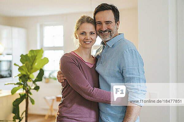 Smiling wife embracing mature man at home