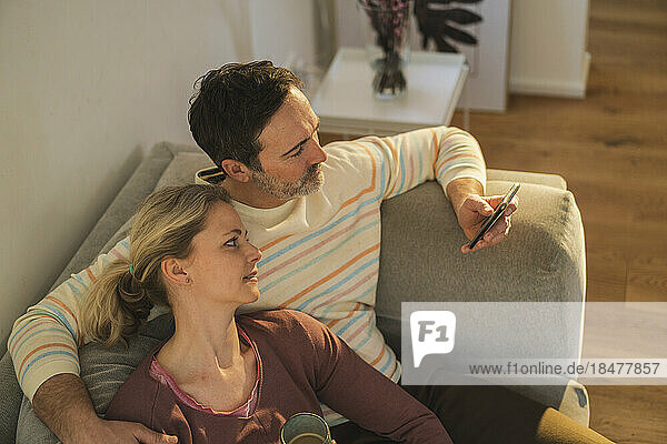 Mature man using mobile phone sitting with woman on sofa at home