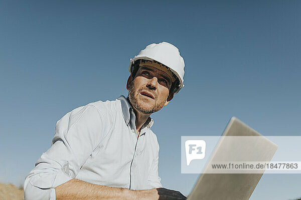 Thoughtful mature architect with laptop sitting in front of blue sky