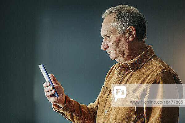 Senior man using smart phone by wall