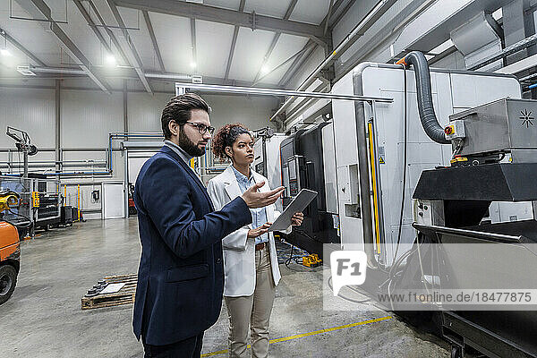 Engineers discussing over machine in factory