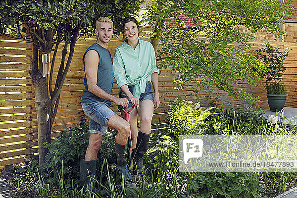 Happy young couple standing with shovel in garden