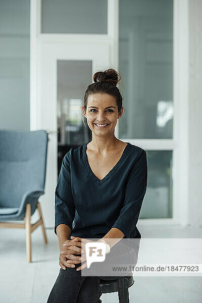 Smiling businesswoman sitting on stool at home office