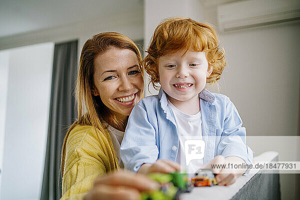Happy mother and son playing with toy cars at home