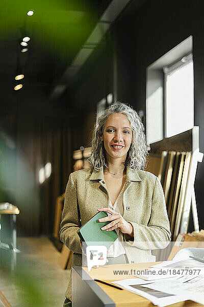 Portrait of smiling female architect holding notebook in office