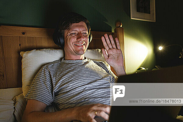 Smiling man waving on video call in bedroom at home