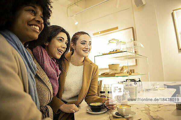 Fröhliche junge Frau mit Freunden  die im Café am Tisch stehen