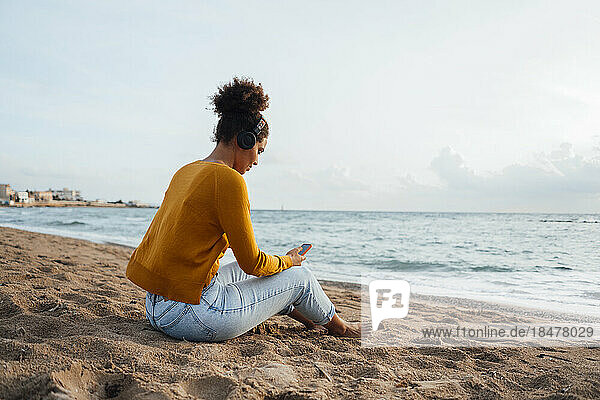 Frau sitzt am Strand und benutzt Smartphone