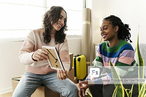 Happy woman showing picture frame to friend at home