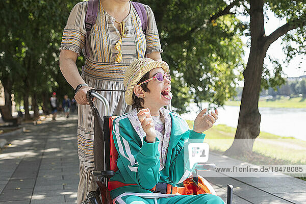 Girl with disability sitting in wheelchair and enjoying with mother on footpath