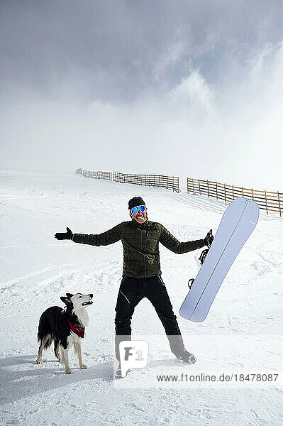 Happy man holding snowboard standing by dog at vacation