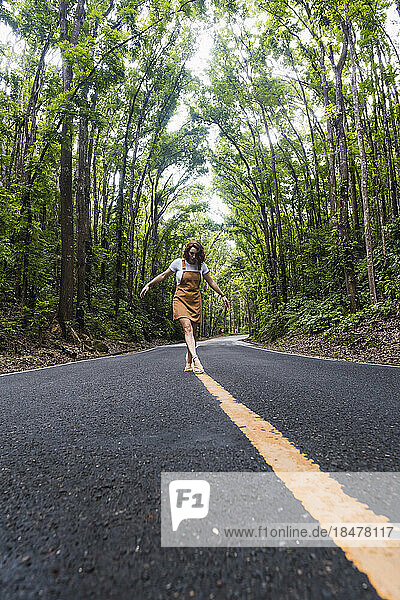Young woman walking on road marking in front of trees