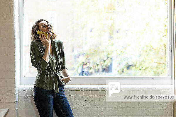 Glückliche Geschäftsfrau  die am Fenster steht und am Smartphone spricht