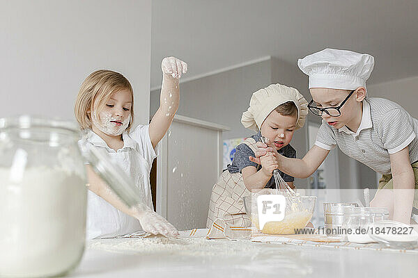Mädchen bereitet Teig zu  während Brüder zu Hause Eier in einer Schüssel mischen