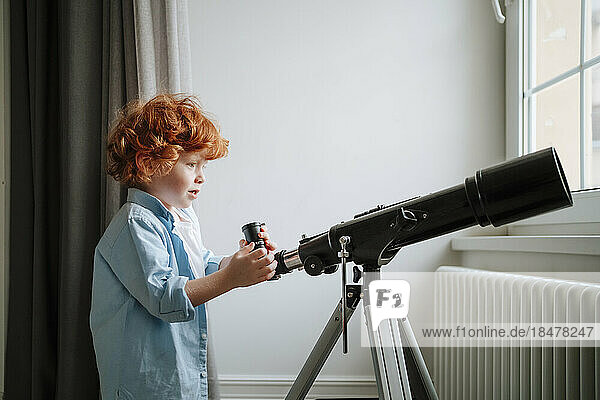 Boy standing near telescope at home