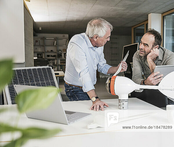 Engineer discussing with colleague over wind turbine rotor at office