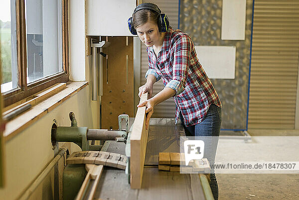 Dedicated craftswoman cutting wood in woodshop
