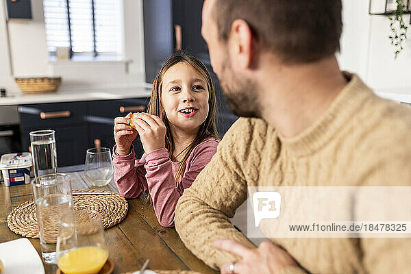 Happy girl having breakfast with father sitting in kitchen