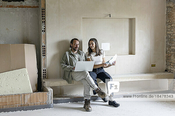 Reifer Mann und Frau benutzen Laptop auf der Baustelle