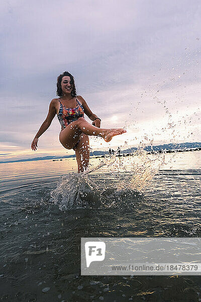 Glückliche junge Frau  die am Strand Wasser spritzt