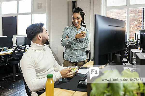 Young businessman eating salad with colleague in lunch break