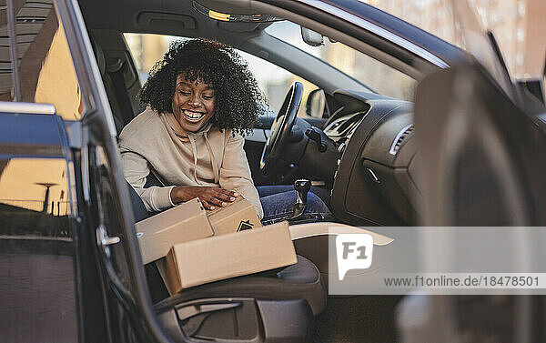 Glückliche junge Frau mit Karton sitzt im Auto