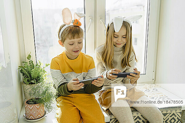 Glückliche Mädchen und Jungen  die zu Hause Videospiele auf dem Smartphone spielen