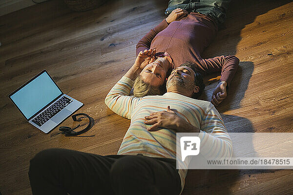 Mature business colleagues lying on floor by laptop at home