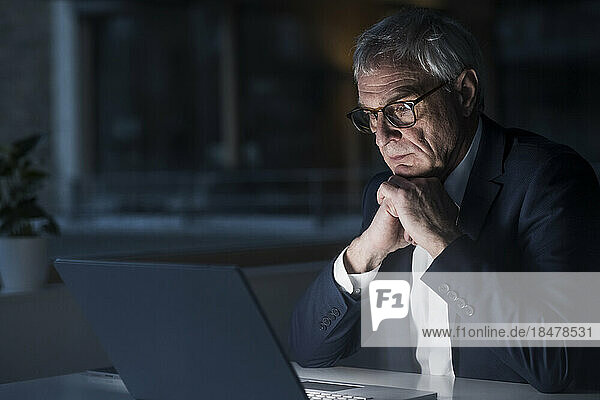 Seriöser leitender Geschäftsmann beobachtet Laptop im Büro und arbeitet bis spät in die Nacht