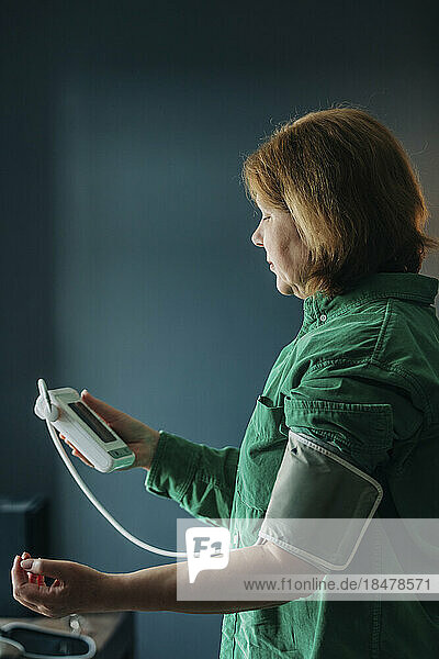 Elderly woman checking blood pressure by wall