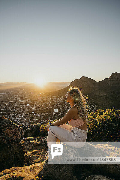 Woman sitting on rock at sunrise